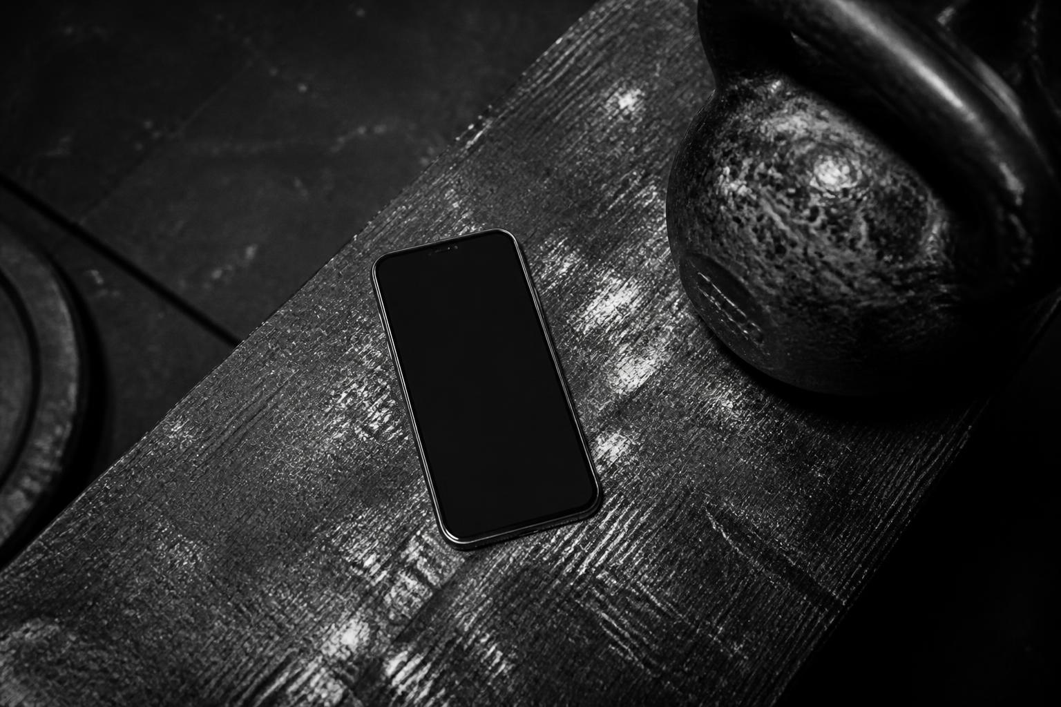 Smartphone resting on a chalked wooden bench beside a black kettlebell