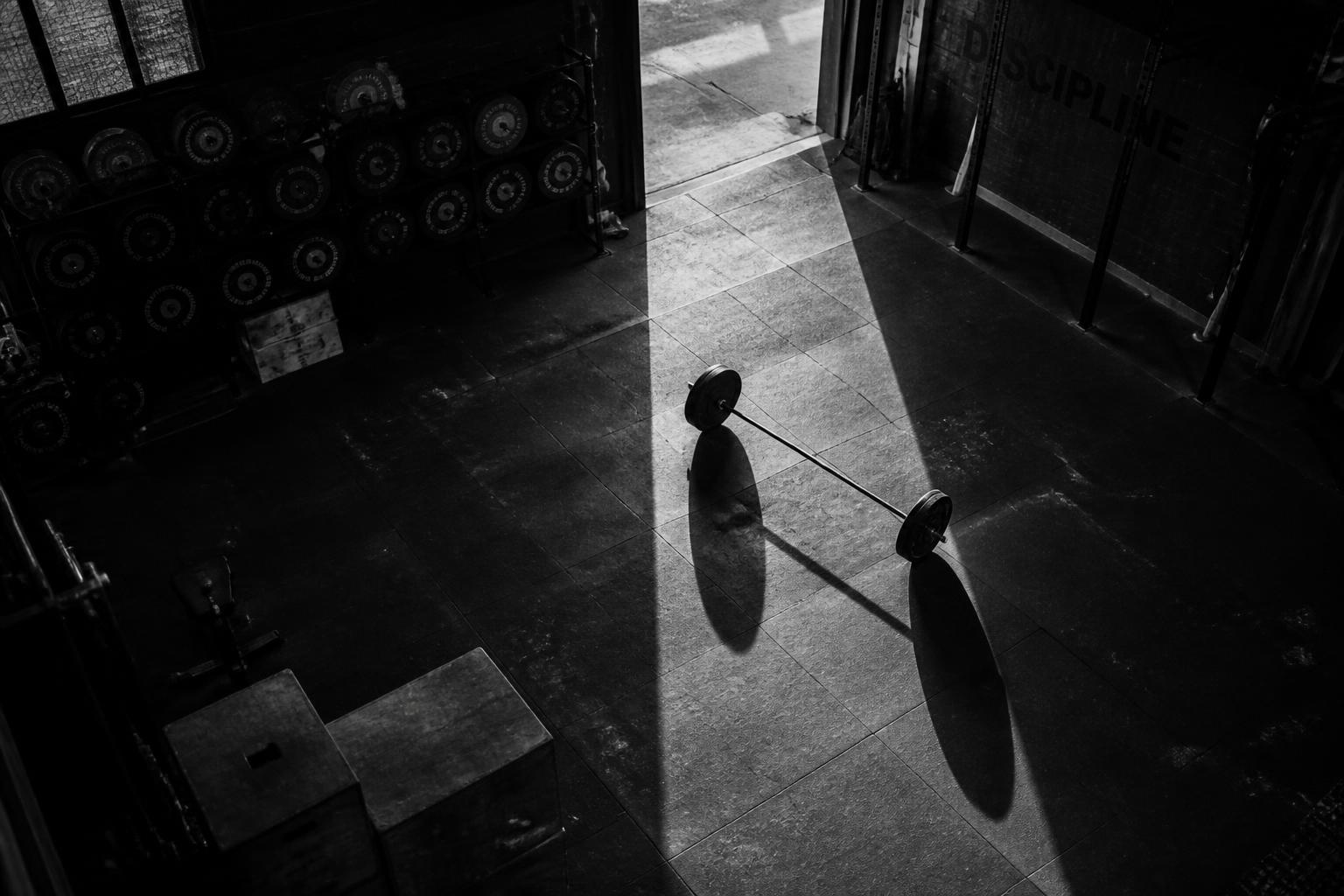 Empty independent gym floor at dawn with a barbell in raking light