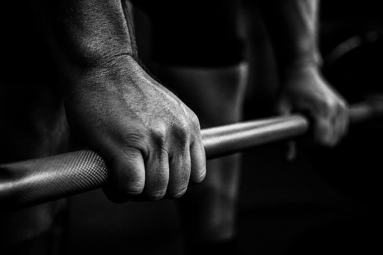 Close-up of a hand gripping the knurling of a steel barbell